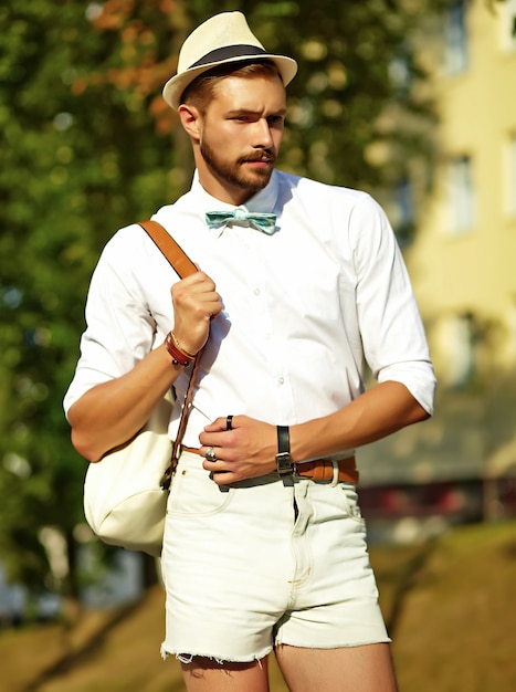 Handsome hipster model man in stylish summer clothes posing  in hat with bag