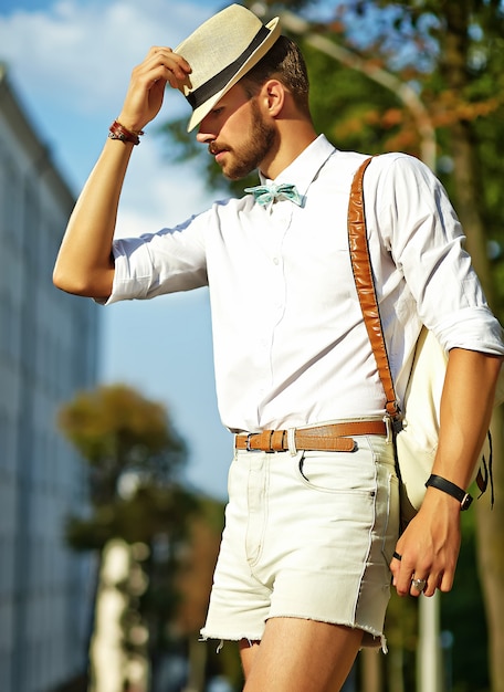 Handsome hipster model man in stylish summer clothes posing  in hat with bag