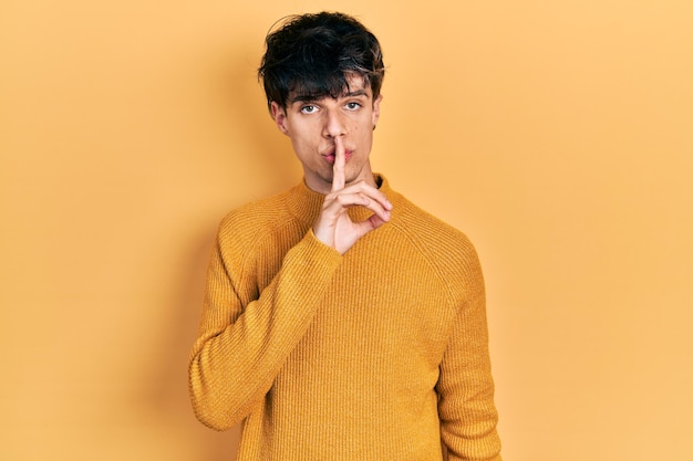 Free photo handsome hipster young man wearing casual yellow sweater asking to be quiet with finger on lips silence and secret concept