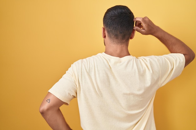 Free photo handsome hispanic man standing over yellow background backwards thinking about doubt with hand on head