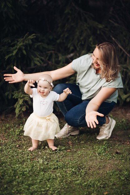 Free Photo handsome little girl with short fair hair and pretty smile in white dress sits on a grass in the park in summer with her mother