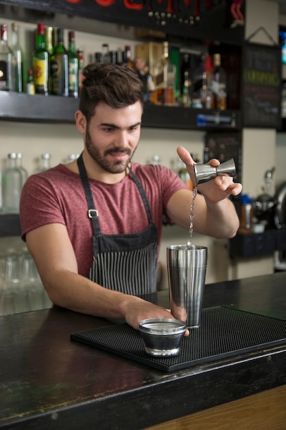 Handsome male bartender pouring cocktail in shaker at bar counter