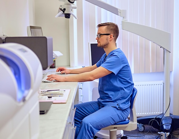 Free Photo handsome male dentis using computer in a room with medical equipment on background.