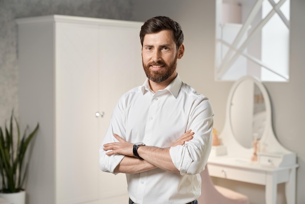 Free photo handsome male entrepreneur wearing white shirt posing standing with crossed arms indoors