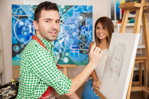 Handsome male Hispanic artist drawing a sketch of a cute young woman in his studio