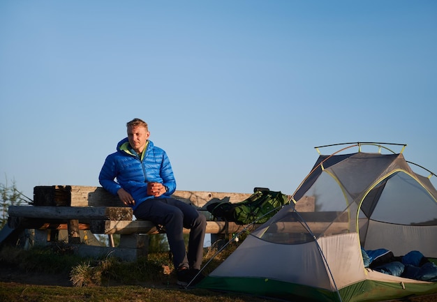 Free Photo handsome male traveler sitting on bench near camp tent