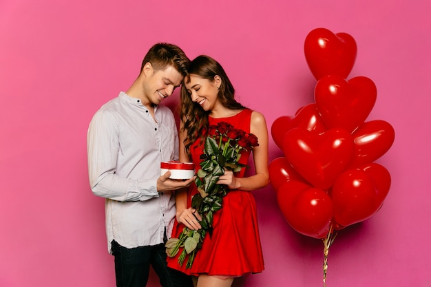 Handsome man and attractive woman looking at box with gift, red roses