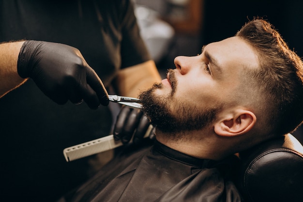 Handsome man cutting beard at a barber shop salon