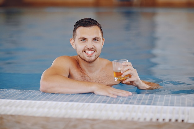 A handsome man floating in a large pool at home and drinking whiskey