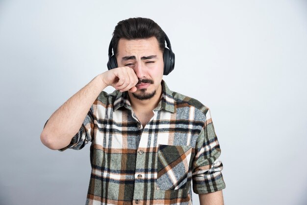 handsome man in headphones crying on white wall.