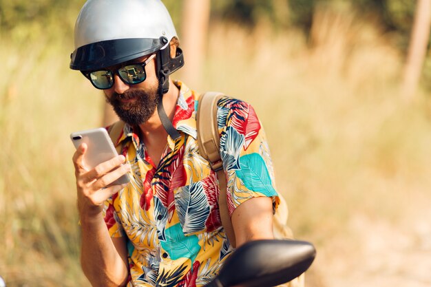 Handsome man in helmet sitting on motorbike and using mobile phone