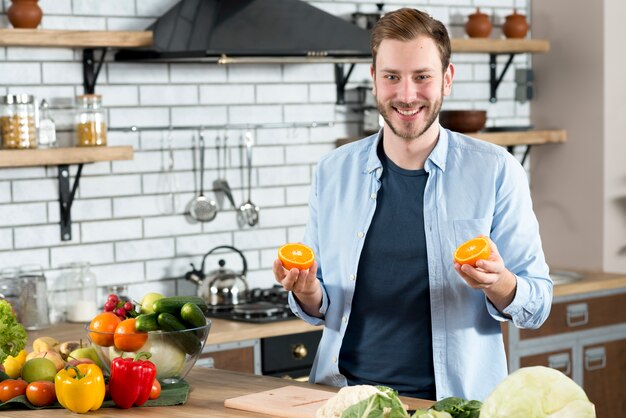 Handsome man holding two oranges slices in kitchen