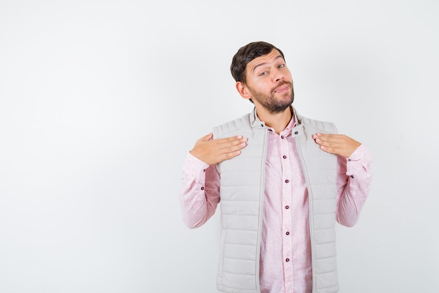 Handsome man keeping hands on chest in vest, shirt and looking confident.