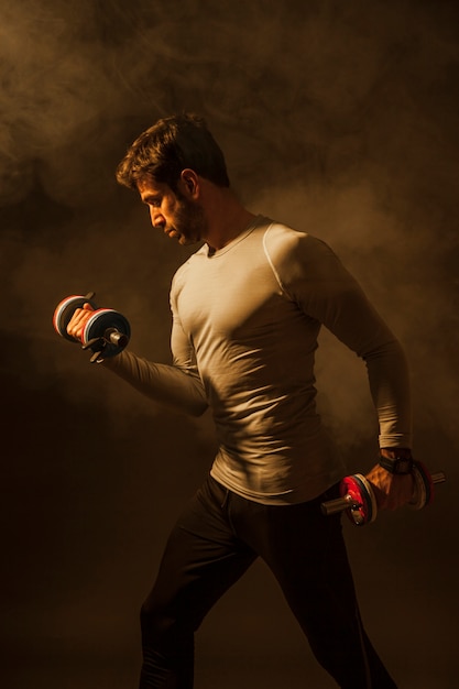 Handsome man lifting dumbbells in smoke