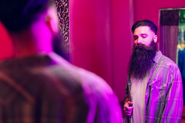 Handsome man looking at himself in the mirror wearing new shirt