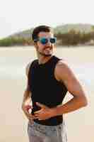 Free photo handsome man outdoors portrait, at beach. wearing black sleeveless t-shirt and shorts. warm sun weather near the sea