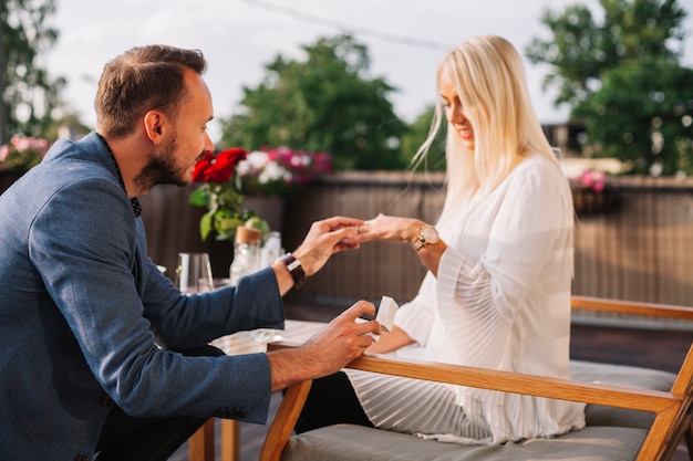 Free photo handsome man placing wedding ring on blonde woman's hand in the restaurant