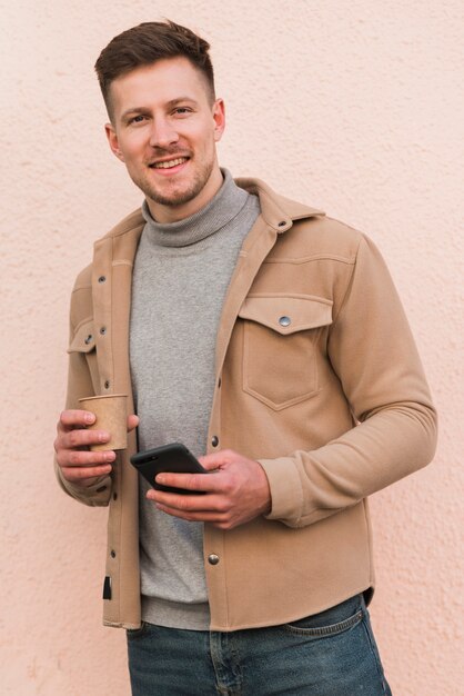 Handsome man posing while holding smartphone and coffee cup