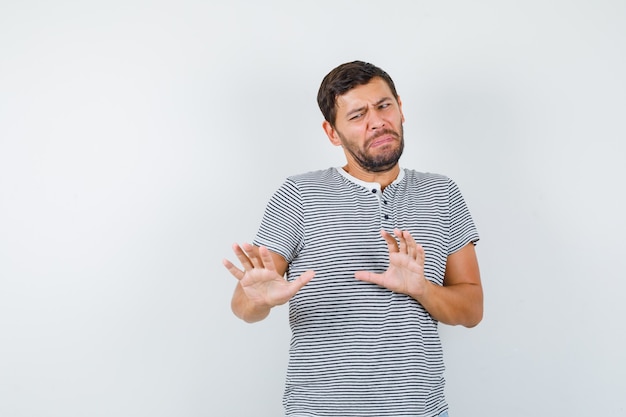 Handsome man raising hands to defend himself in t-shirt and looking scared. front view.