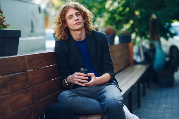 Handsome man sitting on bench with coffe to go