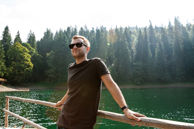 Free photo handsome man smiling, enjoying view of mountains, lake and forest