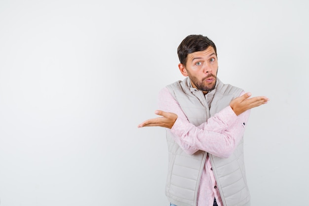 Handsome man in vest, shirt showing helpless gesture and looking shocked ,