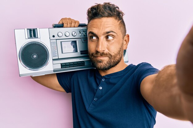 Handsome man with beard holding boombox listening to music smiling looking to the side and staring away thinking