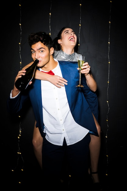 Free photo handsome man with bottle and happy woman on back with glass