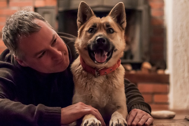 Handsome man with cute dog at home. Attractive man lying on floor with his dog at home in living room. Positive human emotions, facial expression, feelings.