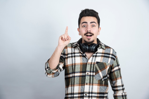 handsome man with headphones pointing over white wall.