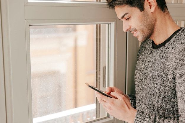 Free photo handsome man with smartphone near window