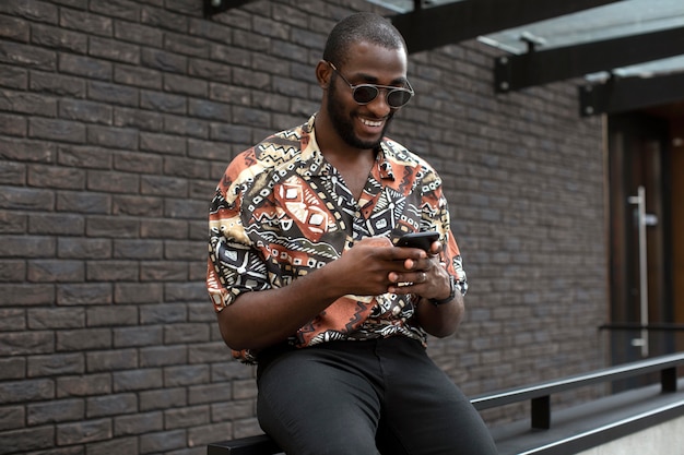 Handsome man with sunglasses using modern smartphone outdoors