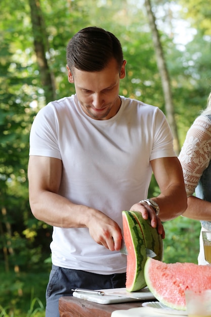 Free photo handsome man with white t-shirt cutting watermelon