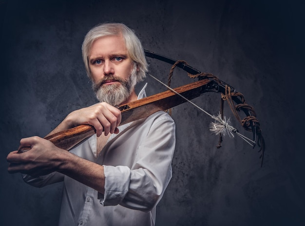 Free Photo handsome mature man with a gray beard and white shirt holding a crossbow on shoulder