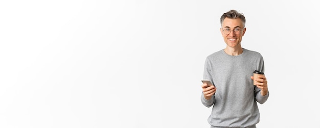 Free photo handsome middleaged man in grey sweater and glasses smiling happy drinking coffee and using mobile p