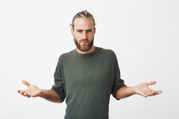 Free photo handsome nordic man with beard and stylish hairdo spreads hands with cynical and mean expression