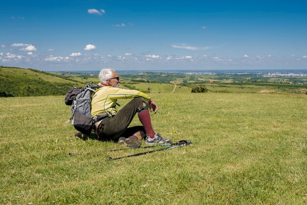 Handsome old man sitting on a meadow and looking relaxing after a hike