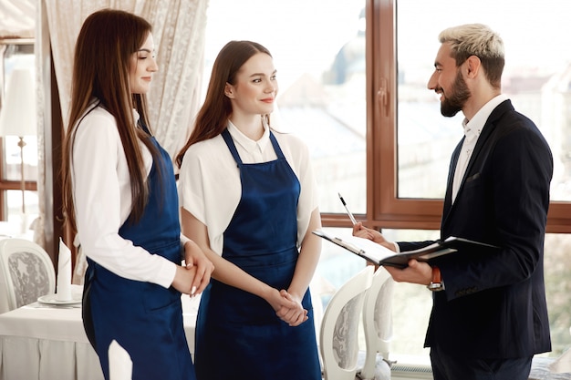 Handsome restaurant manager is talking to waitresses about work process