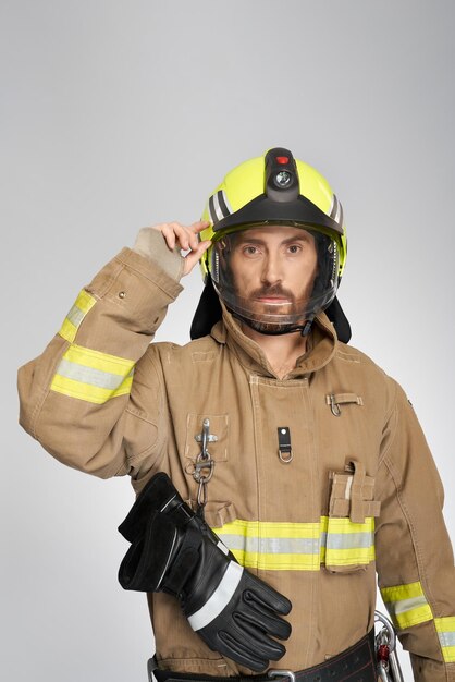 Handsome serious firefighter in uniform putting on protective helmet indoors portrait of bearded