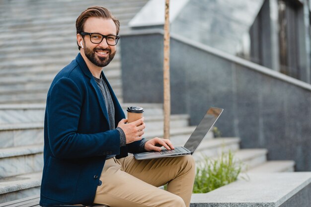 Handsome smiling bearded man in glasses working on laptop