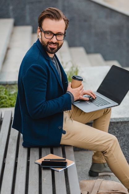 Free photo handsome smiling bearded man in glasses working on laptop