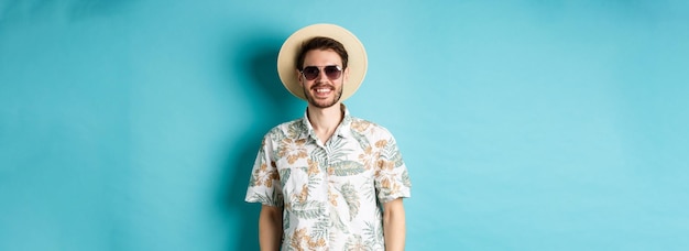 Free Photo handsome smiling guy in sunglasses and summer shirt enjoying vacation on tour standing on blue backg