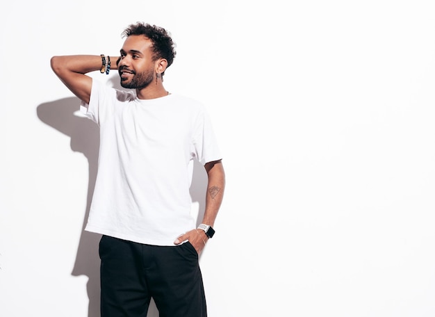 Free photo handsome smiling hipster model sexy unshaven man dressed in summer tshirt and jeans clothes fashion male posing near white wall in studio at sunny day isolated