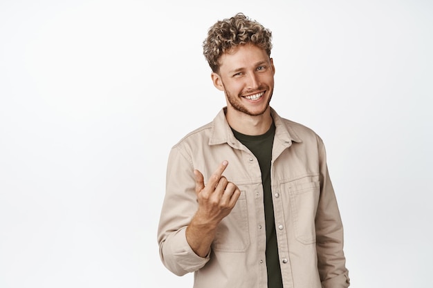 Free Photo handsome smiling man asking to come closer luring you looking friendly and beckon to approach him standing over white background