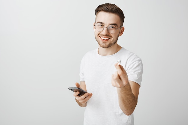 Handsome smiling man in glasses suggest his earphone to listen music together, giving you earphone