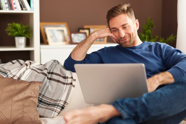 Free photo handsome smiling man relaxing with laptop at home