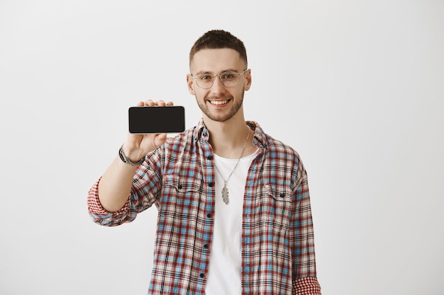 Handsome smiling young guy with glasses posing with his phone