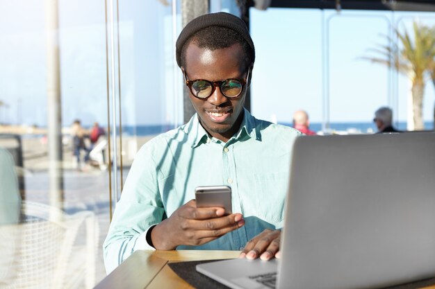 Handsome student wearing stylish accessories typing message on mobile phone