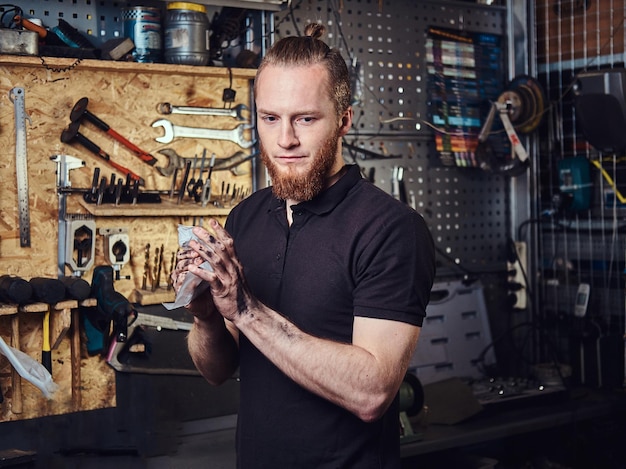 A handsome stylish redhead worker, cleaning his dirty hands after repairing working in a workshop.