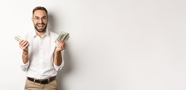 Free photo handsome successful business man counting money rejoicing and smiling standing over white background